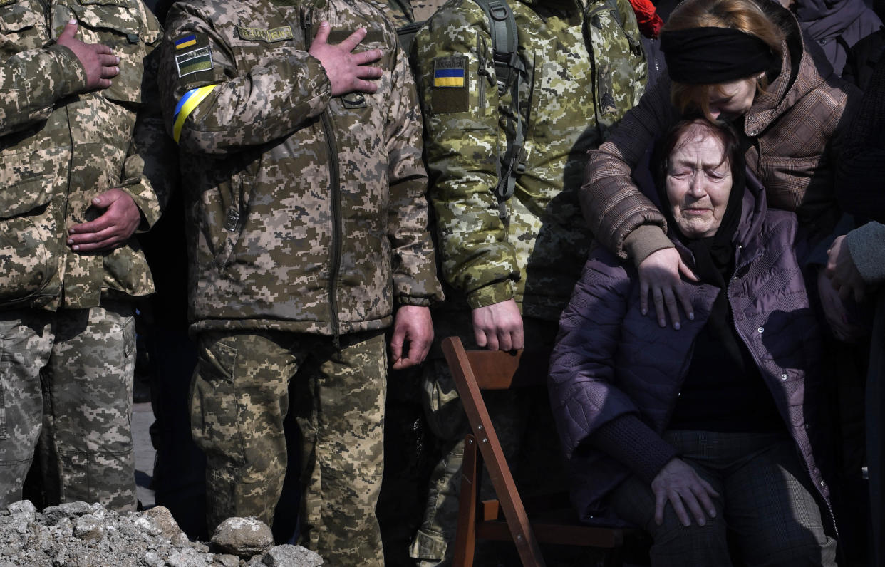 Women crying with a row of soldiers standing behind them.