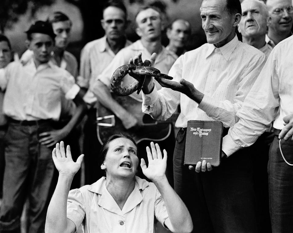 FILE - In this Aug. 22, 1944 file photo, members of the Pentecostal Church of God, a faith healing sect, surround a woman who has "Got the Spirit" as a man holds a snake above her head in Evarts, Ky. Although a Kentucky statute passed in 1940 prohibits the handling of snakes in connection with religious services, this sect revived the ritual after the recent death of a native of the region who was bitten by rattlesnake. (AP Photo)