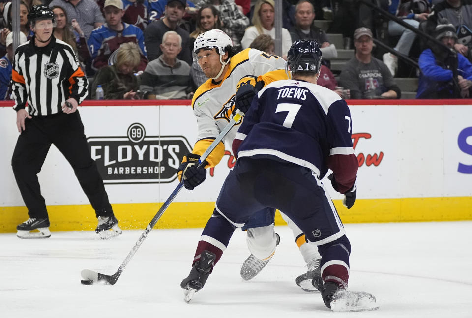 Nashville Predators left wing Kiefer Sherwood, back, launches a shot as Colorado Avalanche defenseman Devon Toews delivers a check in the second period of an NHL hockey game Saturday, March 30, 2024, in Denver. (AP Photo/David Zalubowski)