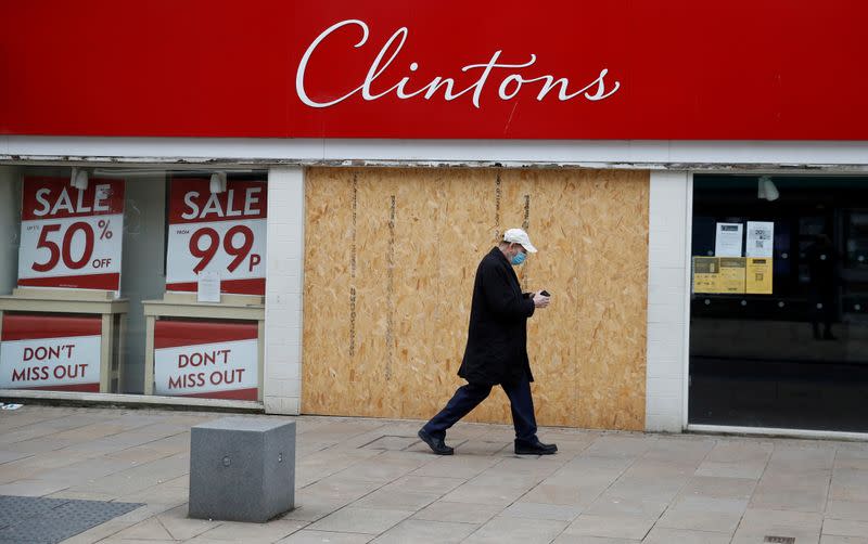 FILE PHOTO: A man wearing a face mask walks past a boarded up retail unit in Preston