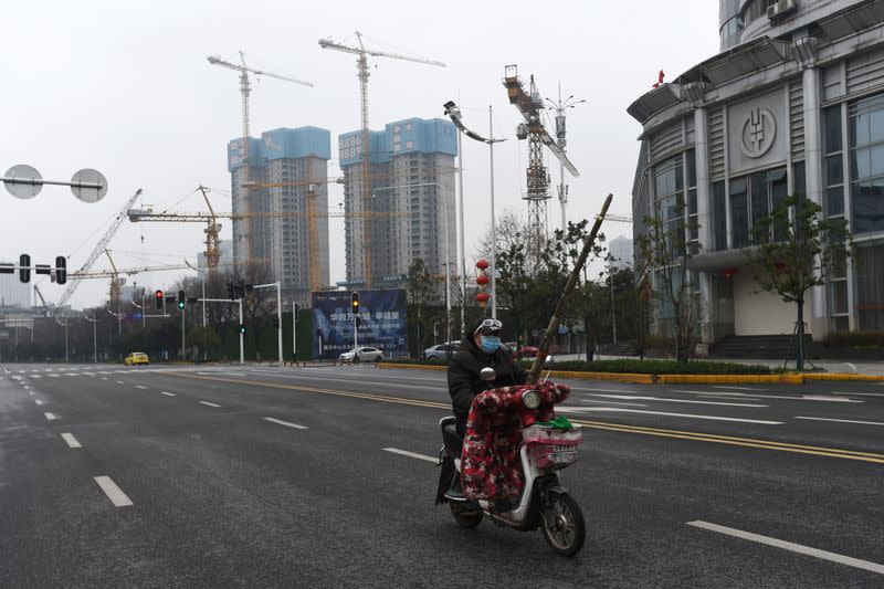 A man with sugar cane rides on an electric bicycle on a street in Wuhan