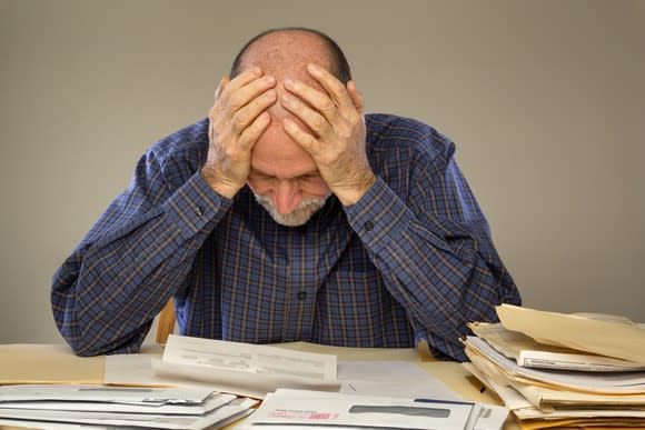 Frustrated-looking man with his hands on his head looking over stacks of financial documents.