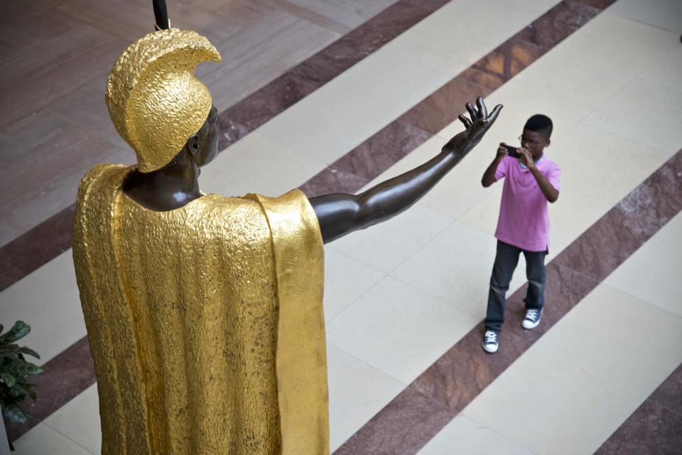 A young tourist snaps a photo beneath the towering bronze statue of King Kamehameha, the 18th century Hawaiian warrior-monarch, at the Capitol Visitors Center in Washington, Tuesday, July 2, 2013. American sculptor Thomas R. Gould depicted Kamehameha in his gilded robe and loincloth. It is the heaviest statue in the National Statuary Hall Collection. (AP Photo/J. Scott Applewhite)