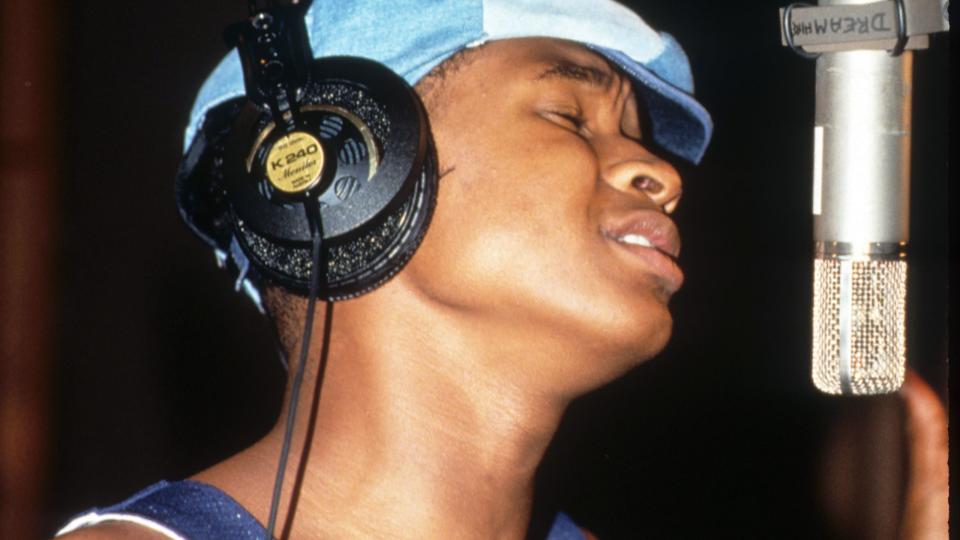 usher wearing a blue shirt and hat, singing into a microphone while wearing earphones