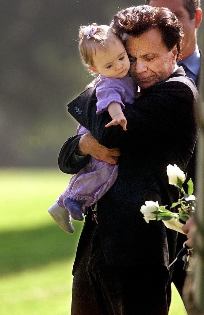 Actor Robert Blake hugs his 11-month-old daughter, Rose Lenore Sophie Blake, as she leans down to grab a white rose picked from the coffin bearing her slain mother, Bonny Lee Bakley, during a brief funeral ceremony in Los Angeles on May 25, 2001. 