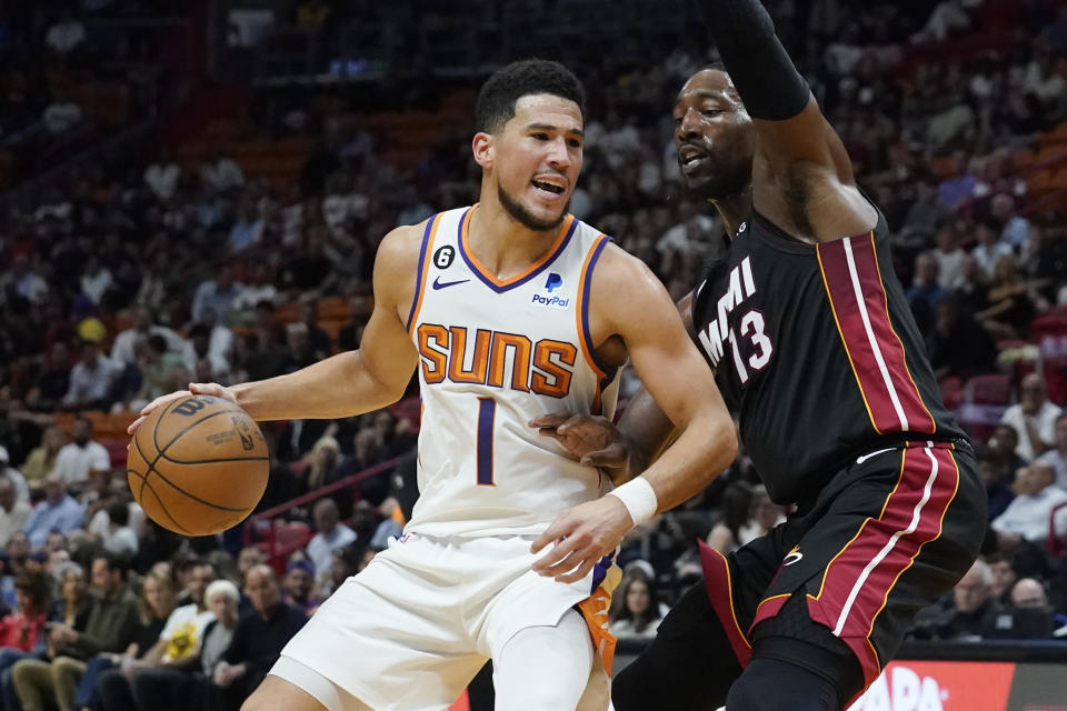 Phoenix Suns guard Devin Booker (1) dribbles as Miami Heat center Bam Adebayo (13) defends during the first half of an NBA basketball game Monday, Nov. 14, 2022, in Miami. (AP Photo/Marta Lavandier)