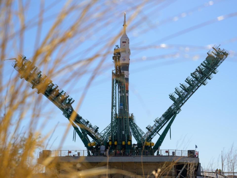two giant green scaffolded arms raise up toward a standing rocket to support it with blue sky in the background