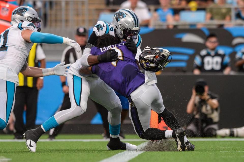 Panthers defensive end Brian Burns, center, knocks off the helmet of Baltimore quarterback Tyler Huntley in August on a tackle.