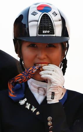 South Korea's Chung Yoo-ra, then known as Chung Yoo-yeon, bites her gold medal as she poses after winning the equestrian Dressage Team competition at the Dream Park Equestrian Venue during the 17th Asian Games in Incheon September 20, 2014. REUTERS/Kim Hong-Ji/Files