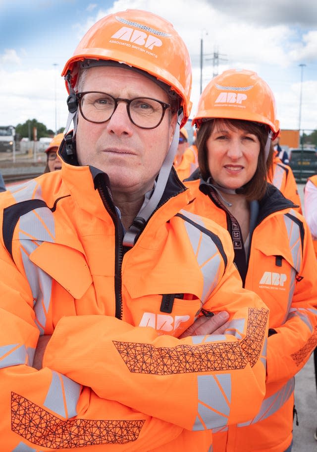 Sir Keir Starmer, arms folded, with Rachel Reeves, both wearing orange hard hats and hi vis jackets