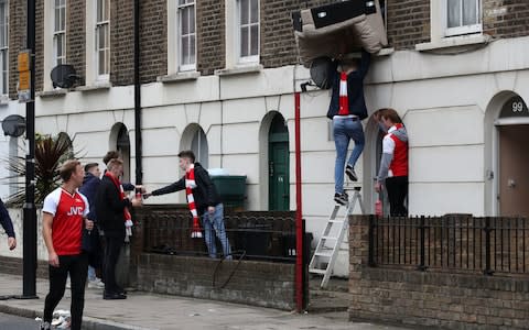 Arsenal fans help a nearby resident to get a sofa in through him Window before the Premier League match at the Emirates Stadium - Credit: PA