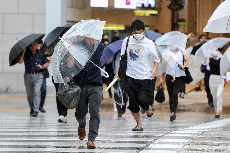 Pedestrians try to shield from wind and rain as they cross the street in front of Osaka Station on August 15, 2023, as Tropical Storm Lan hit the main island of Honshu overnight.