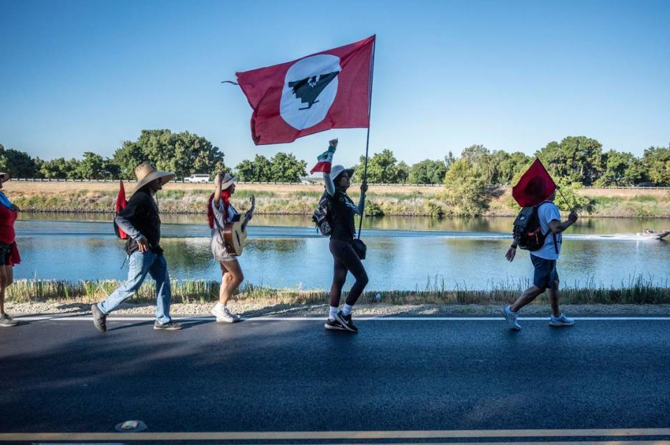 Flor Martínez Zaragoza, centro, de San José, levanta el puño mientras sostiene una bandera durante la marcha de simpatizantes y miembros del sindicato United Farm Workers que se dirigía a Sacramento caminando a lo largo del río Sacramento, después de hacer una parada en Walnut Grove, el miércoles 24 de agosto de 2022.