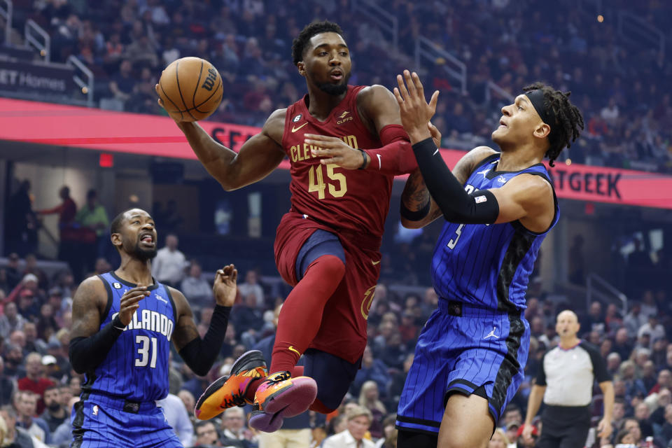 Cleveland Cavaliers guard Donovan Mitchell (45) passes between Orlando Magic forward Paolo Banchero (5) and guard Terrence Ross (31) during the first half of a NBA basketball game, Wednesday, Oct. 26, 2022, in Cleveland. (AP Photo/Ron Schwane)