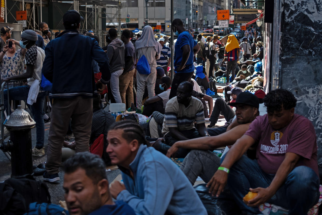 Dozens of migrants stand or sit on the sidewalk outside the Roosevelt Hotel.