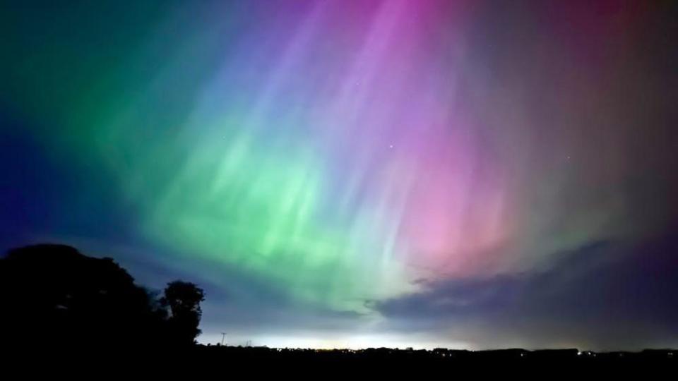 Beams of green and pink shine from aurora down in the night sky
