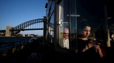 A commuter uses her mobile phone as a Circular Quay to Cockatoo Island ferry passes under the Sydney Harbour Bridge, November 24, 2015. REUTERS/Jason Reed