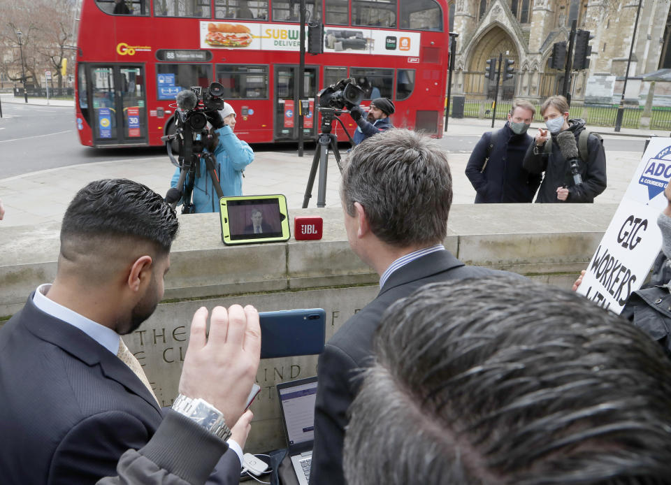 Uber drivers of the (ADCU), App Drivers & Couriers Union, listen to the court decision on a tablet computer outside the Supreme Court in London, Friday, Feb. 19, 2021. The U.K. Supreme Court ruled Friday that Uber drivers should be classed as “workers” and not self employed.(AP Photo/Frank Augstein)