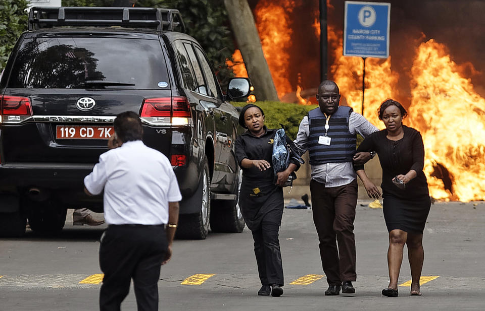Security forces help civilians flee the scene as cars burn behind, at a hotel complex in Nairobi, Kenya Tuesday, Jan. 15, 2019. Terrorists attacked an upscale hotel complex in Kenya's capital Tuesday, sending people fleeing in panic as explosions and heavy gunfire reverberated through the neighborhood. (AP Photo/Ben Curtis)