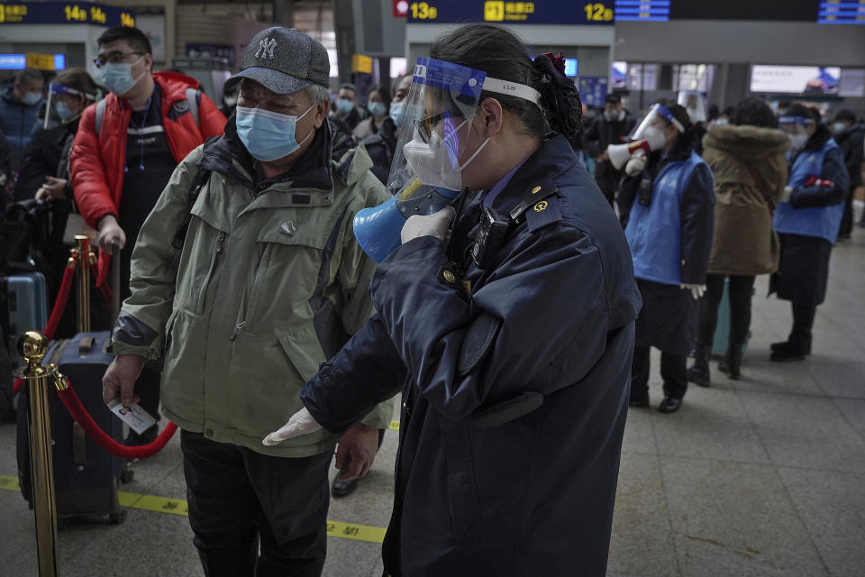 A worker wearing a face mask and face shield to help curb the spread of the coronavirus uses a loud speaker to ask a masked passenger to keep distancing in the line at the South Train Station in Beijing, Thursday, Jan. 28, 2021. Efforts to dissuade Chinese from traveling for Lunar New Year appeared to be working. Beijing's main train station was largely quiet on the first day of the travel rush and estimates of passenger totals were smaller than in past years. (AP Photo/Andy Wong)