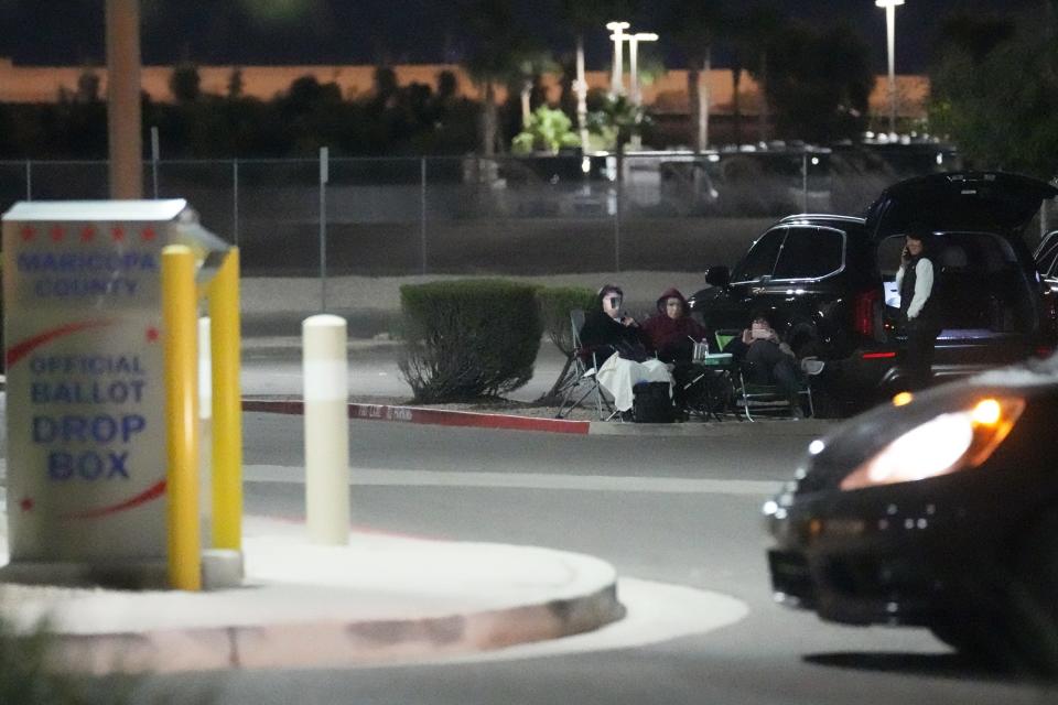 A group of people watch a vehicle approach a Maricopa County early ballot drop box on Oct. 24, 2022, in Mesa.