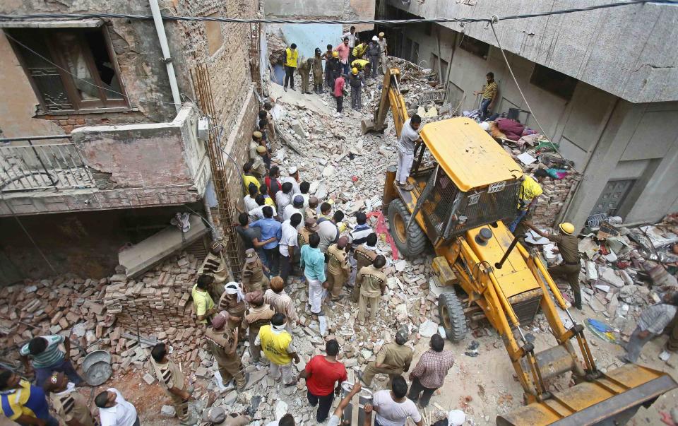 Rescue workers and volunteers stand at the site of a collapsed building in New Delhi