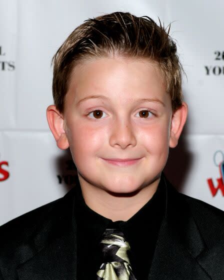 A young man in a black button up shirt and a tie smiling