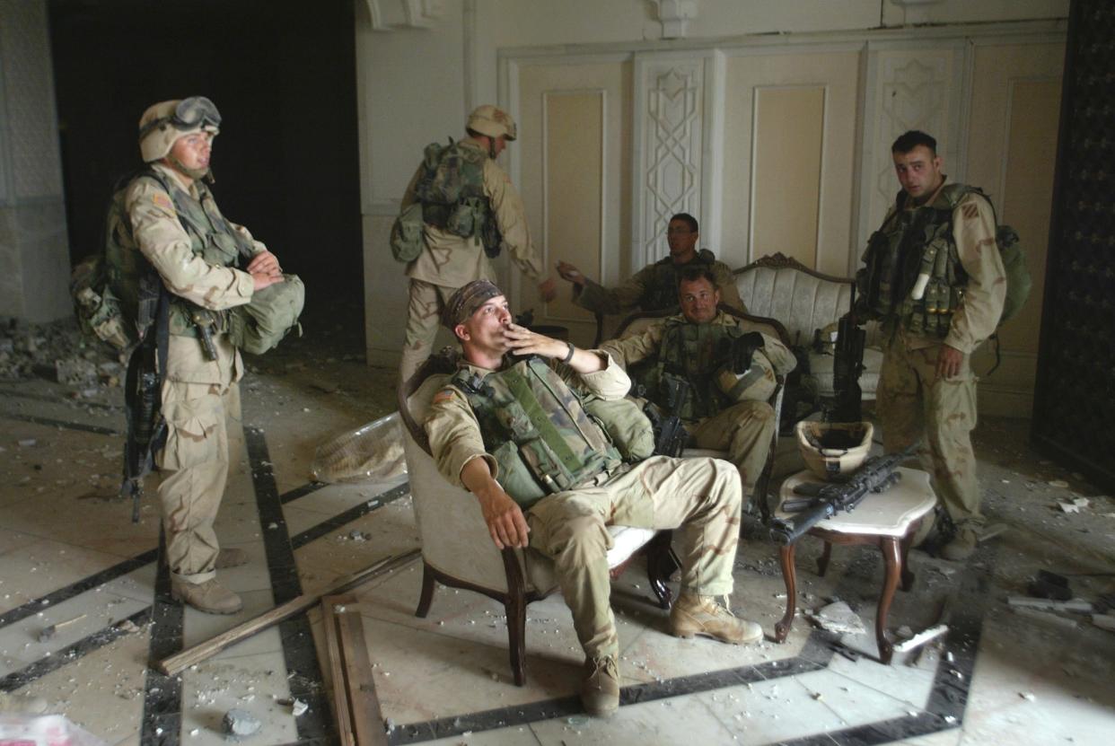 Three comrades surround Sgt. Chad Touchett, center, and two other soldiers who have made themselves at home on upholstered formal armchairs and settees on a marble floor littered with chunks of plaster.