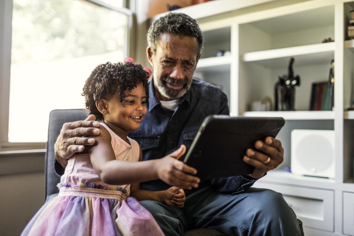 A granddaughter shows her grandfather how to use a tablet.