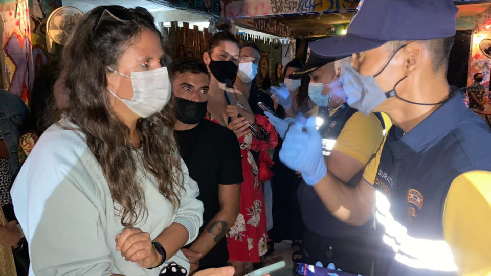 In this Tuesday, Jan. 26, 2021, Thai immigration officers talk to people at a bar on Koh Phangan island, Surat Thani province, southern Thailand. Police raided a party at a bar on a popular resort island in southern Thailand and arrested 89 foreigners for violating coronavirus regulations, officials said Wednesday. (Police Investigation Team of Surat Thani Immigration via AP)