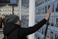 A woman touches a picture as she stands next to the Memory Wall of Fallen Defenders of Ukraine in Russian-Ukrainian War on Ukrainian Volunteer Day in Kyiv, Ukraine, Tuesday, March 14, 2023. (AP Photo/Andrew Kravchenko)
