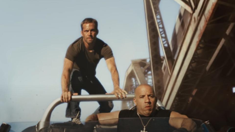 Vin Diesel driving a car off the cliff with Paul Walking on the top of the car in Fast Five.