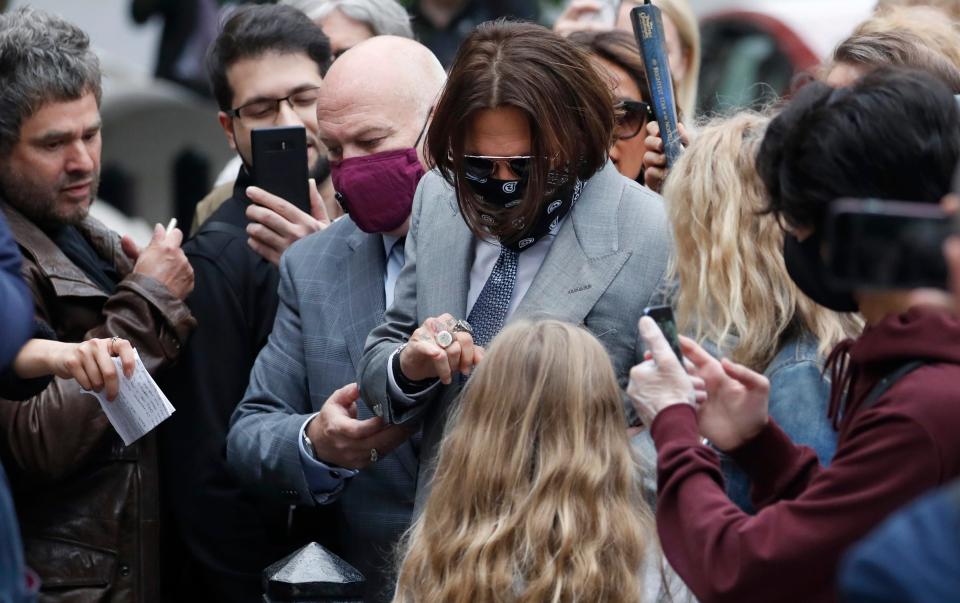 A masked Johnny Depp is surrounded by fans as he arrives for day eight of the trial in his libel suit in London, July 16, 2020.