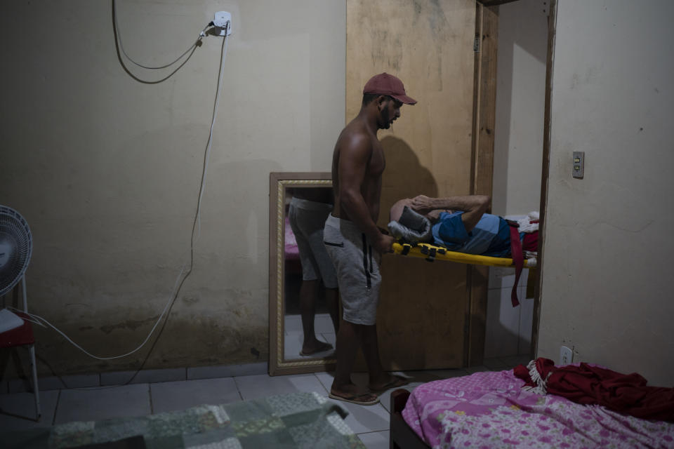 A man helps as Mobile Emergency Care Service (SAMU) workers carry an elderly COVID-19 patient to an ambulance in Duque de Caxias, Rio de Janeiro state, Brazil, Wednesday, April 7, 2021. (AP Photo/Felipe Dana)