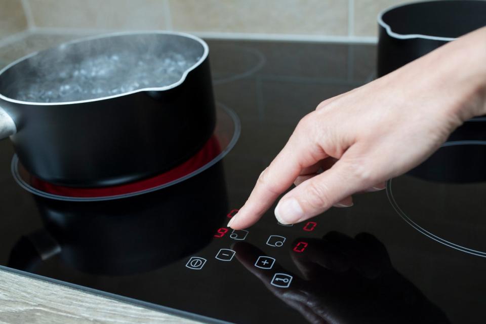 Person presses a button on an electric cooktop while a pot of water boils on one burner.