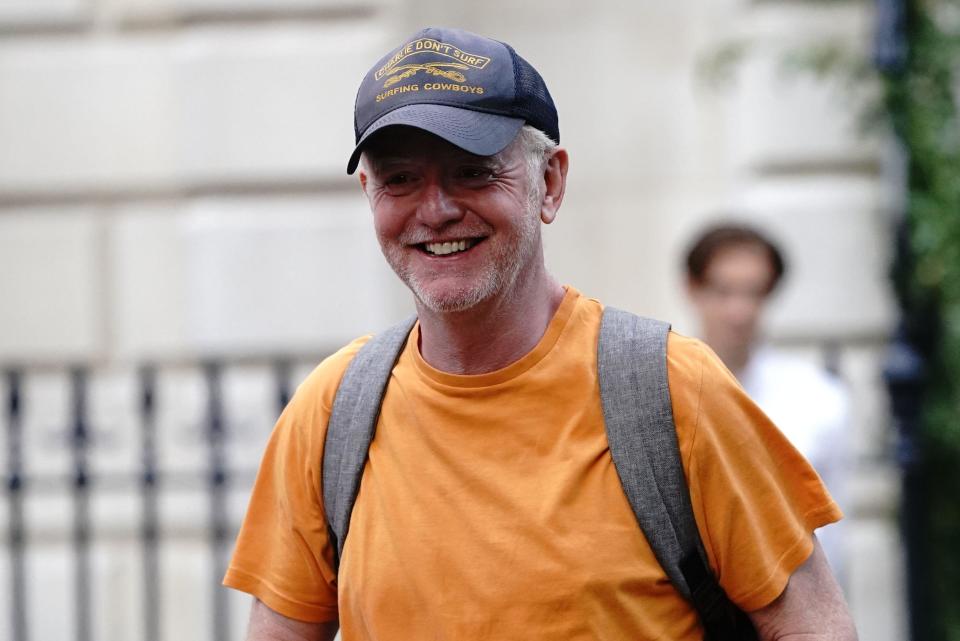 Broadcaster Chris Evans smiles outdoors, wearing a bright orange T-shirt and a navy cap