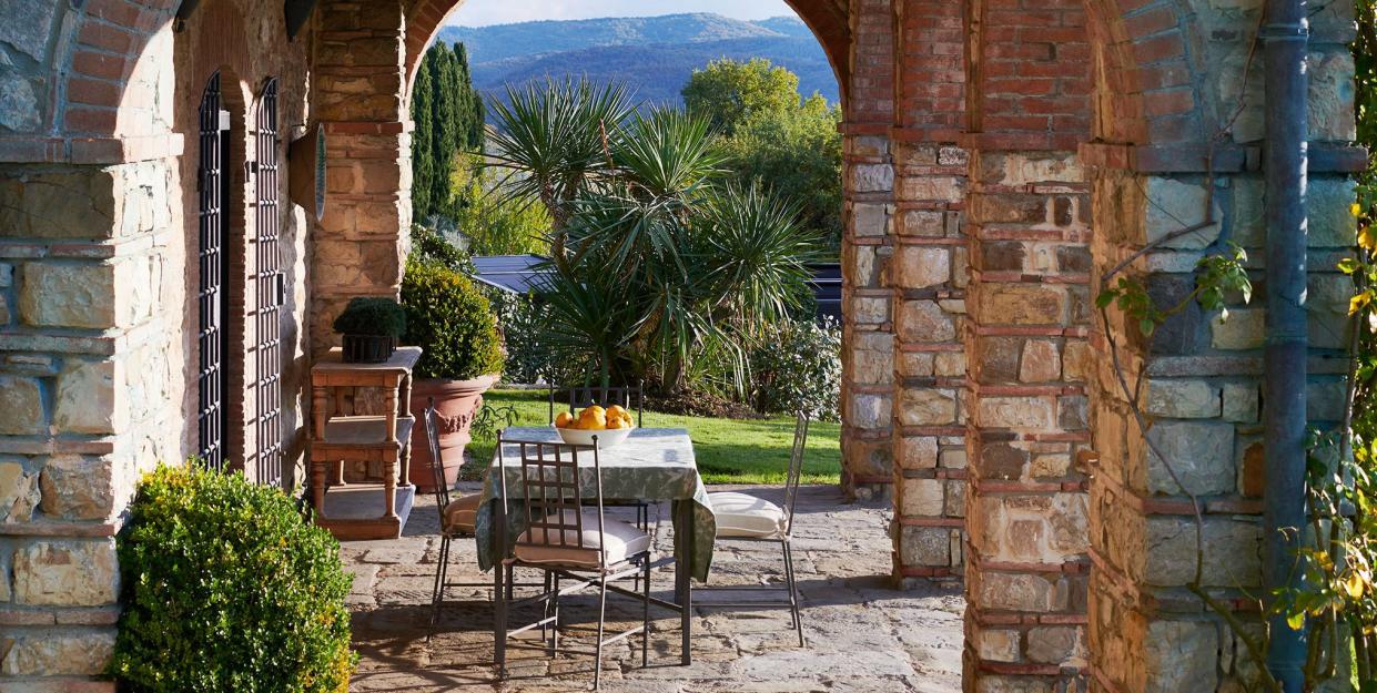 straight view through an arched linnae with table and chairs on stone looking out over the green lush tuscan countryside