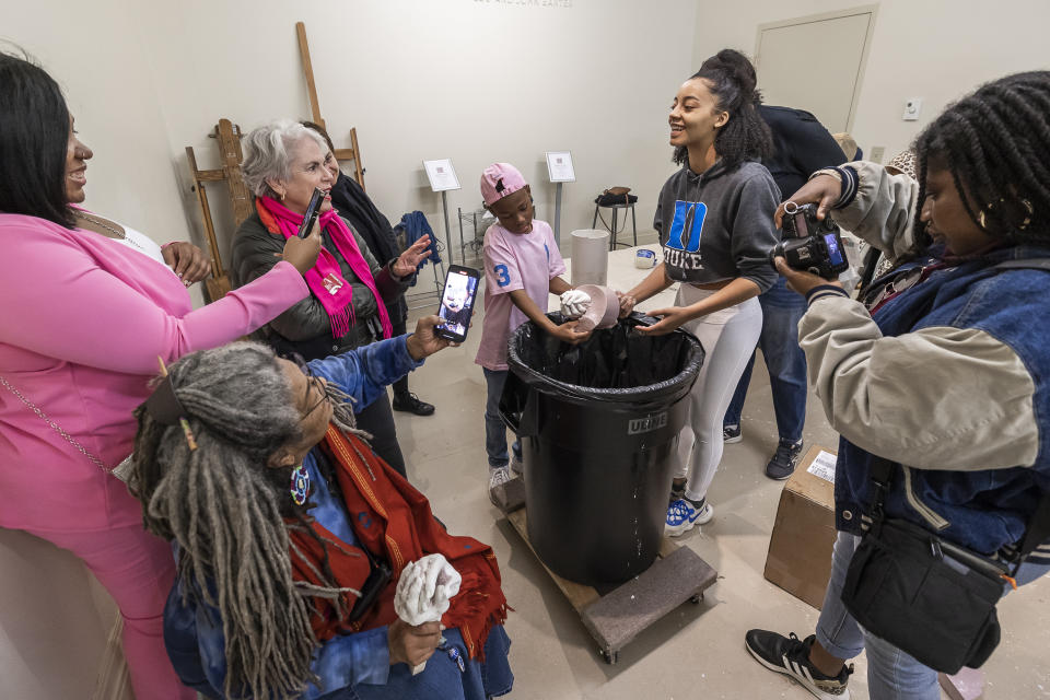 Volunteers and family members take pictures of Princeton Dingle, 9, from Goose Creek, S.C., as his cast hands are seen for the first time in Charleston, S.C., Saturday, Feb. 18, 2023. Artist Stephen Hayes will use the mold to make a memorial for 36 enslaved people whose bodies were unearthed in Charleston in 2013 during a construction project for the Gaillard Center. (AP Photo/Mic Smith)