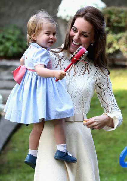 Kate Middleton wearing a white chloe outfit holding her Princess Charlotte wearing a preppy blue dress