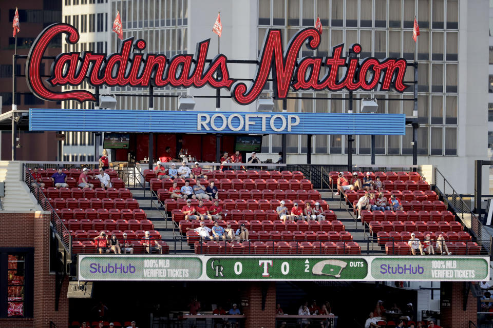 A few fans watch the action from seats across the street outside Busch Stadium as the St. Louis Cardinals and Pittsburgh Pirates play an opening day baseball game without fans in the stadium Friday, July 24, 2020, in St. Louis. (AP Photo/Jeff Roberson)