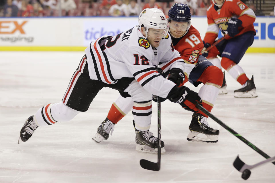 Chicago Blackhawks left wing Alex DeBrincat (12) and Florida Panthers defenseman Mike Matheson (19) fight for the puck during the first period of an NHL hockey game against the, Saturday, Feb. 29, 2020, in Sunrise, Fla. (AP Photo/Brynn Anderson)