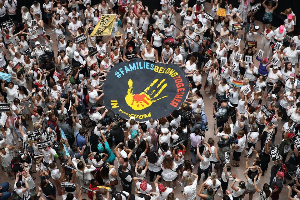 A crowd of women in white hold up a giant banner reading #FamiliesBelongTogether