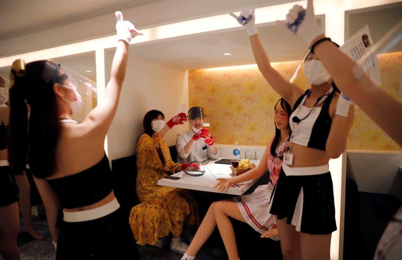 Customers sitting on a table where a mannequin is placed for social distancing amid the coronavirus disease (COVID-19) outbreak, toast with waitresses at the cheerleader-themed restaurant 'Cheers One' in Tokyo