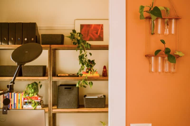 Wall vases hang in orange room with view of shelving in neutral room.