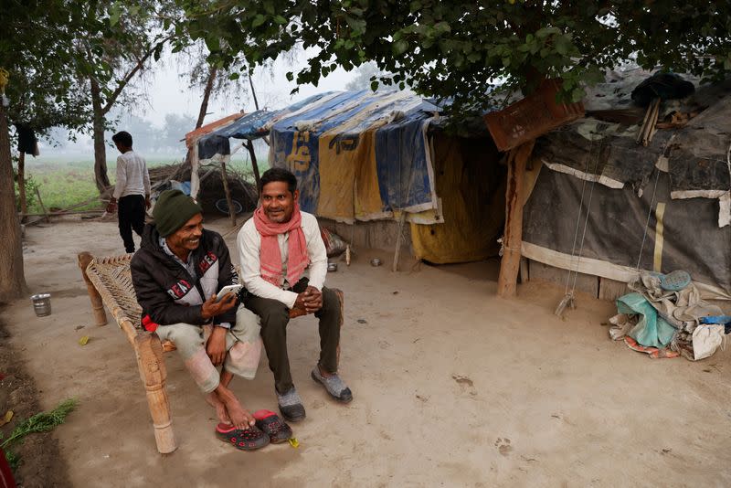 Totaram Maurya,45, a construction worker, talks to his friend outside his house on the field on the Yamuna floodplains on a smoggy morning in New Delhi