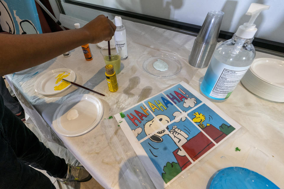 Jesse McCarty, 14, cleans his brush next to diagram of a "Peanuts" mural he is helping to paint that will be placed in the outpatient pediatric floor of One Brooklyn Health at Brookdale Hospital, Thursday, Oct. 1, 2020, in the Brooklyn borough of New York. The virus pandemic won't stop Charlie Brown, Snoopy or the "Peanuts" gang from marking an important birthday and they're hoping to raise the spirits of sick kids while they celebrate. The beloved comic marks its 70th anniversary this week with new lesson plans, a new TV show and a philanthropic push that includes donating "Peanuts" murals for kids to paint in 70 children's hospitals around the globe, from Brooklyn to Brazil. (AP Photo/Mary Altaffer)