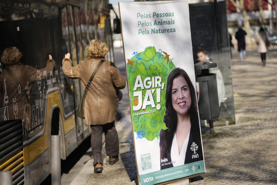 A woman walks past an election poster for the People, Animals, Nature Party at a bus stop in Lisbon, Thursday, Jan. 20, 2022. Portuguese voters go to the polls Sunday, two years earlier than scheduled after a political crisis over a blocked spending bill brought down the country's minority Socialist government and triggered a snap election. (AP Photo/Armando Franca)