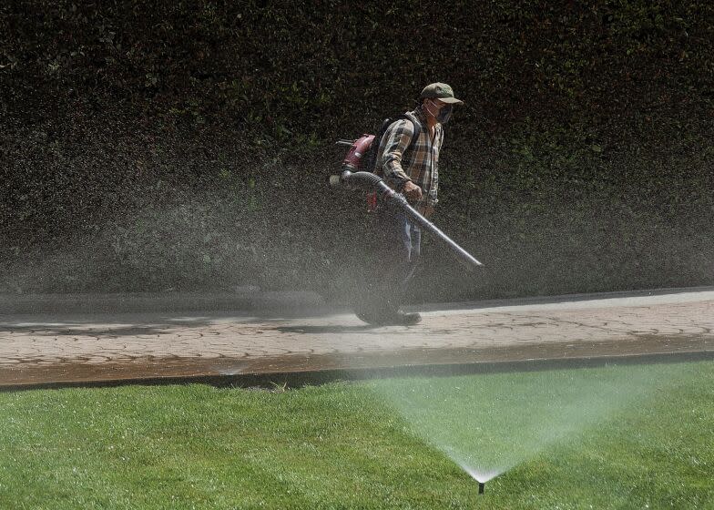 LOS ANGELES, CA-APRIL 28, 2022: A gardener uses a leaf blower while cleaning a driveway as sprinklers water the front lawn of a home on Sunset Blvd. near Carmelina Ave. in Los Angeles. (Mel Melcon / Los Angeles Times)