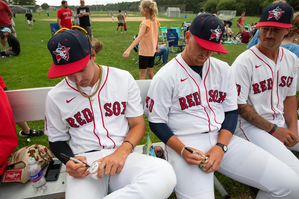 Red Sox players sign autographs on baseballs after a game.