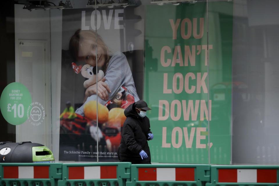 A man wearing a face mask and disposable gloves walks past the front window of the Primark clothing store on Oxford Street during England's second coronavirus lockdown, in London, Monday, Nov. 23, 2020. British Prime Minister Boris Johnson has announced plans for strict regional measures to combat COVID-19 after England's second lockdown ends Dec. 2, sparking a rebellion by members of his own party who say the move may do more harm than good. (AP Photo/Matt Dunham)